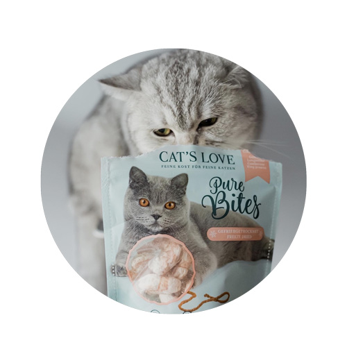 Katze sitz hinter einer Packung Pure Bites Garnelen und richt an der Verpackung
