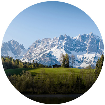 Landscape image with a green meadow, trees and mountains in the background