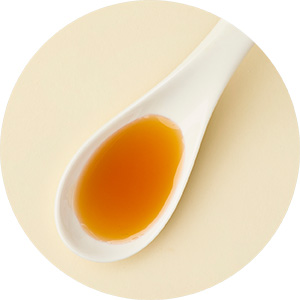 Beige background on which lies a white spoon filled with an oil
